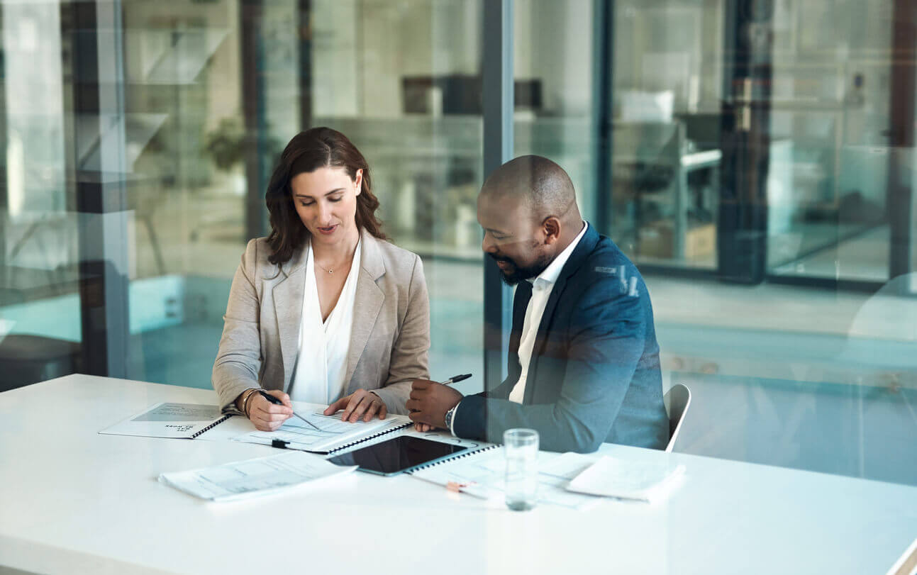 Dois profissionais em reunião empresarial analisando documentos e preenchendo checklist de conformidade em uma sala de escritório moderna.