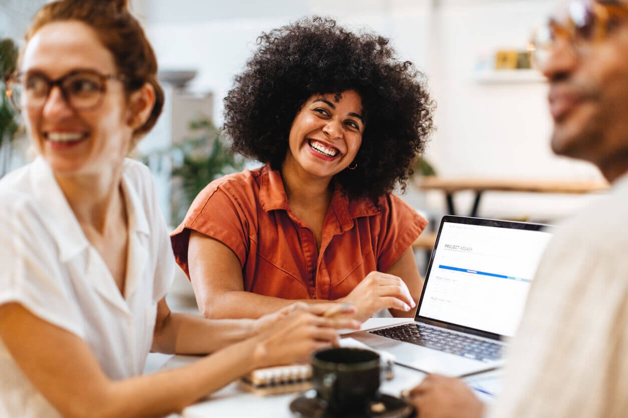 Equipe reunida em ambiente de trabalho colaborativo com mulher sorrindo ao centro usando notebook