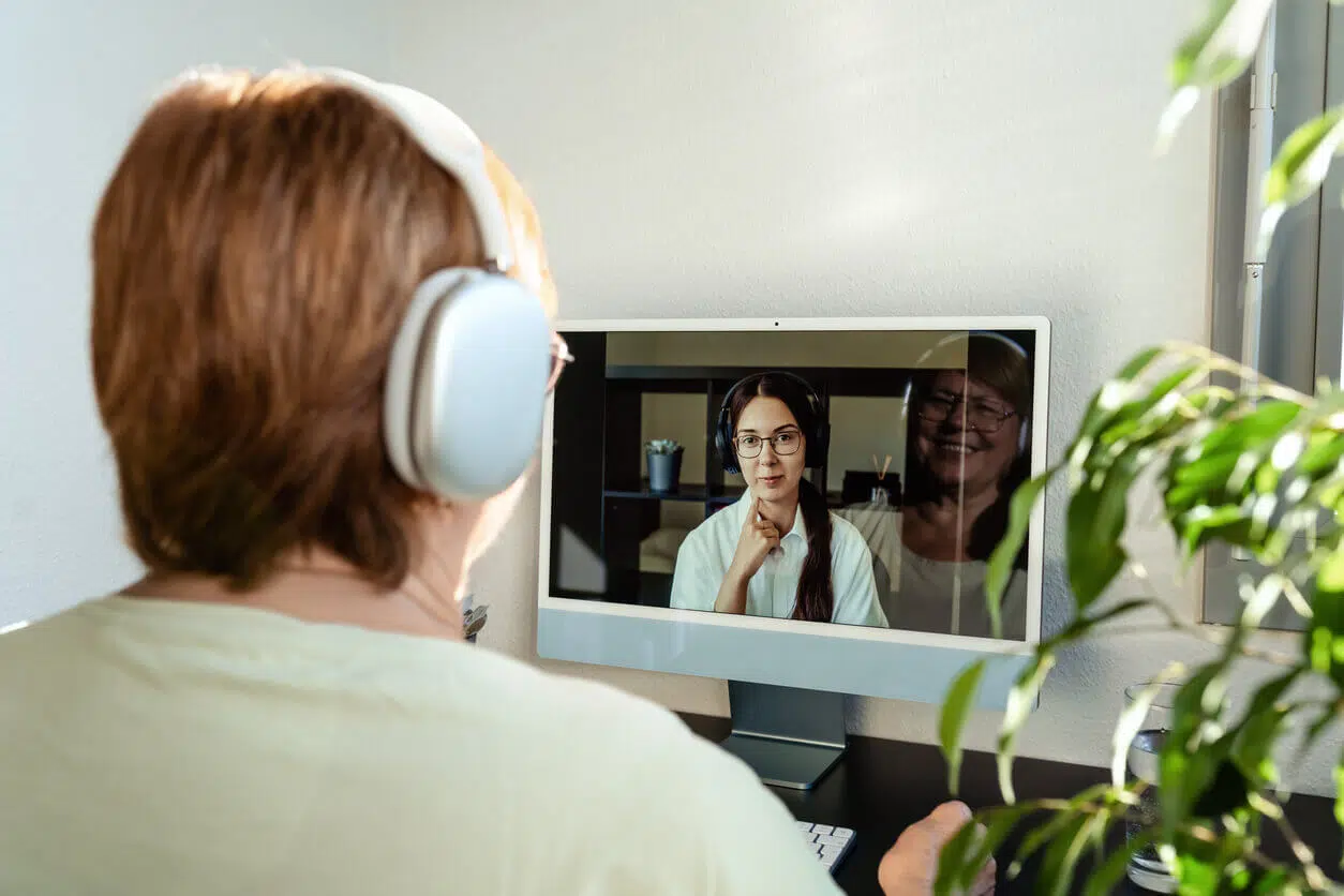Pessoa em videoconferência com psicóloga usando fones de ouvido, representando uma sessão de psicoterapia digital no ambiente de trabalho.