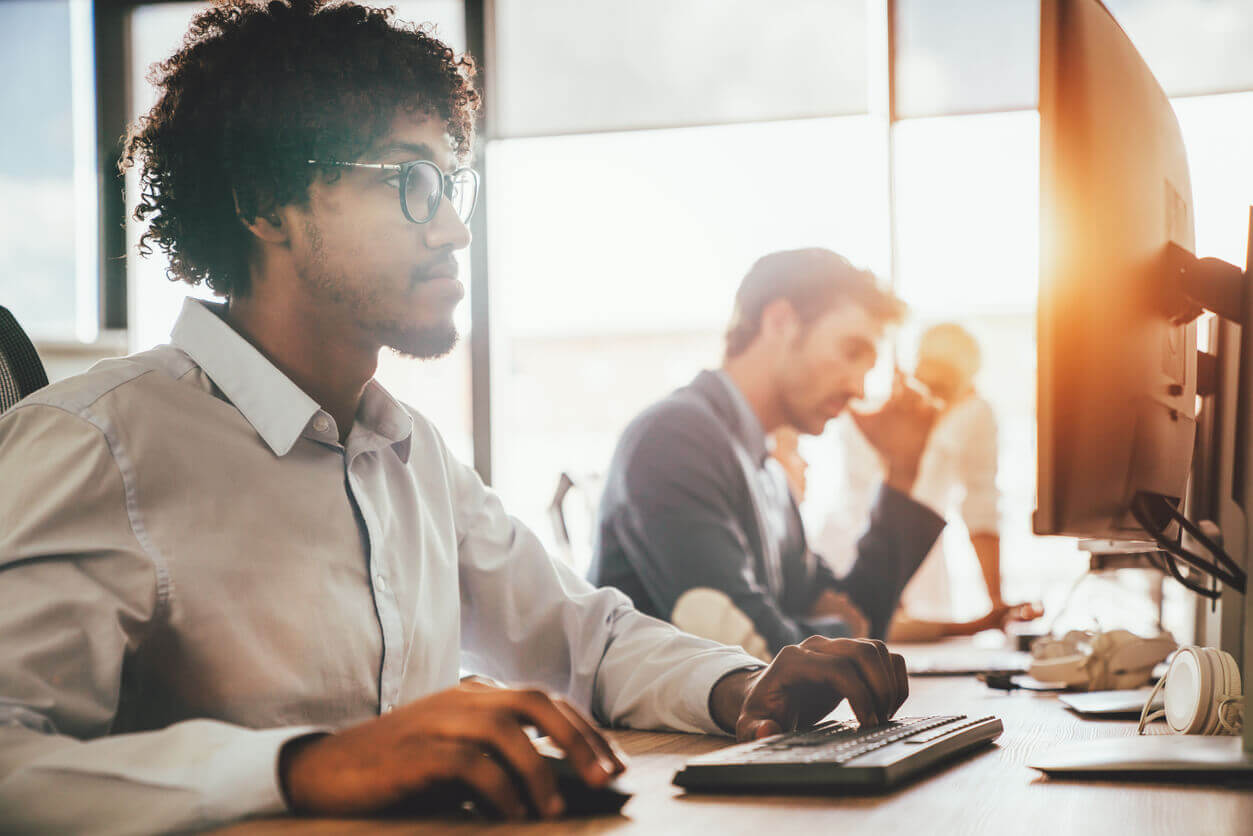 Profissional trabalhando em frente ao computador em ambiente corporativo, representando o uso da tecnologia para atender às exigências da NR-1 no ambiente de trabalho.