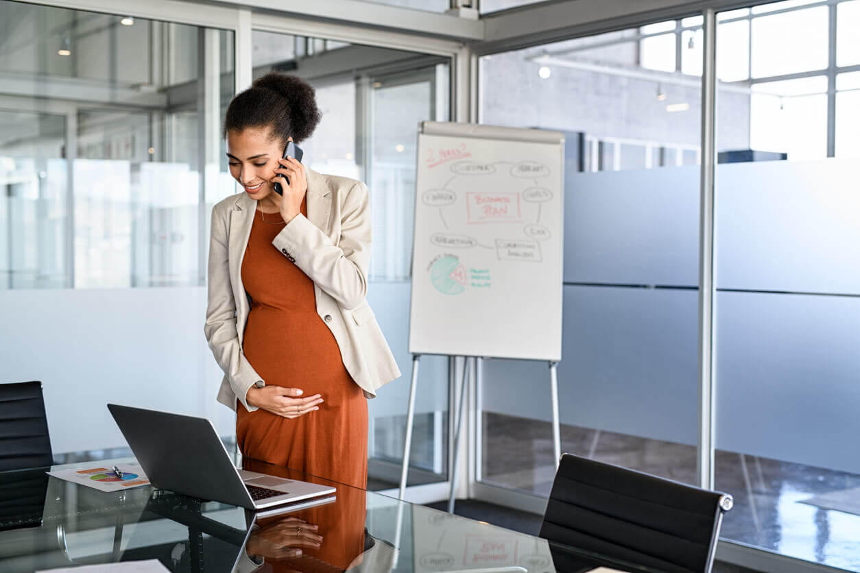 Gestante sorrindo ao telefone em ambiente corporativo, representando mães solo e os desafios da adaptação no trabalho após a licença-maternidade
