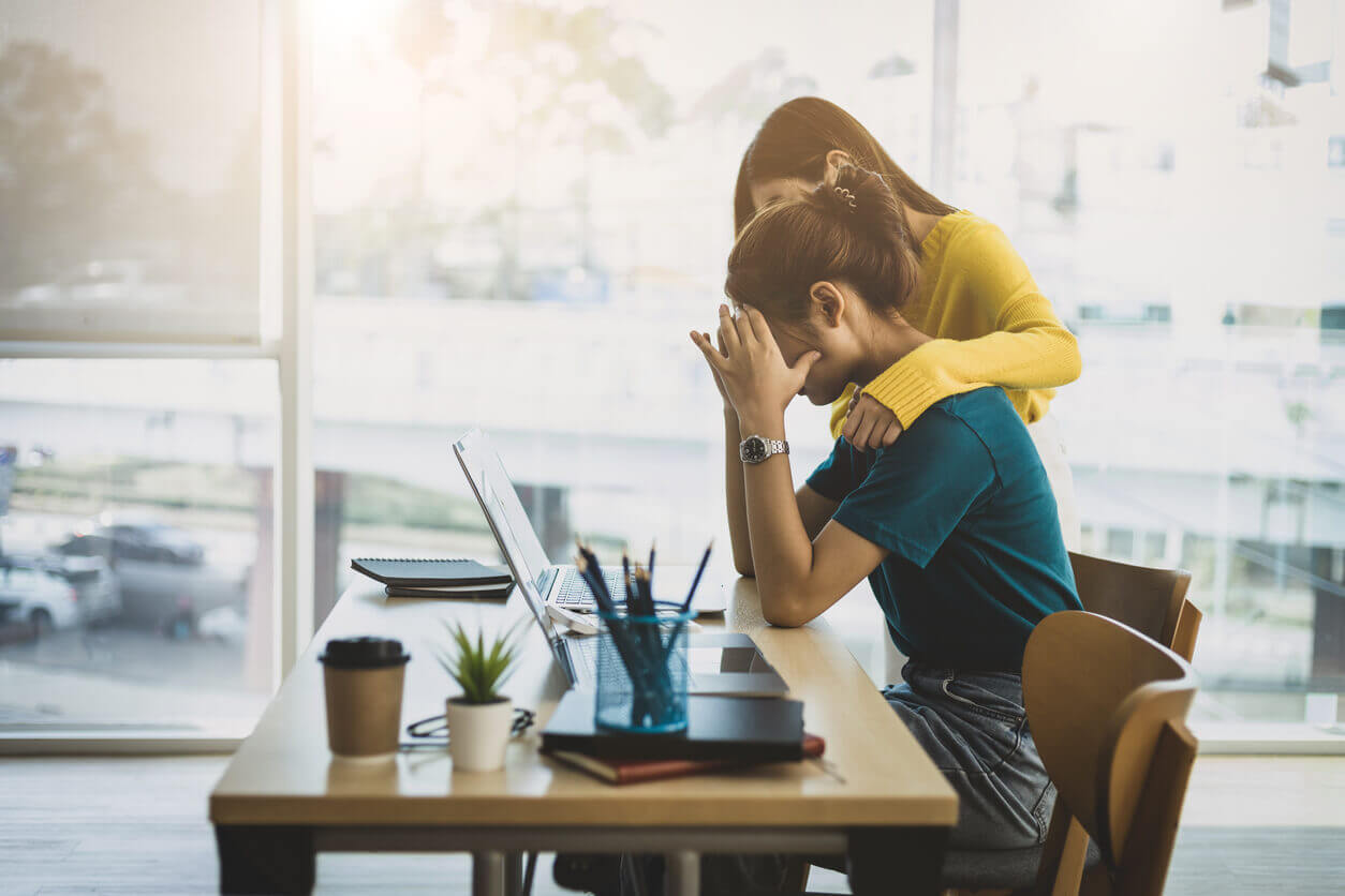 Colaboradora com sinais de esgotamento emocional sendo consolada no ambiente de trabalho, representando a importância da NR-1 atualizada na prevenção do burnout.