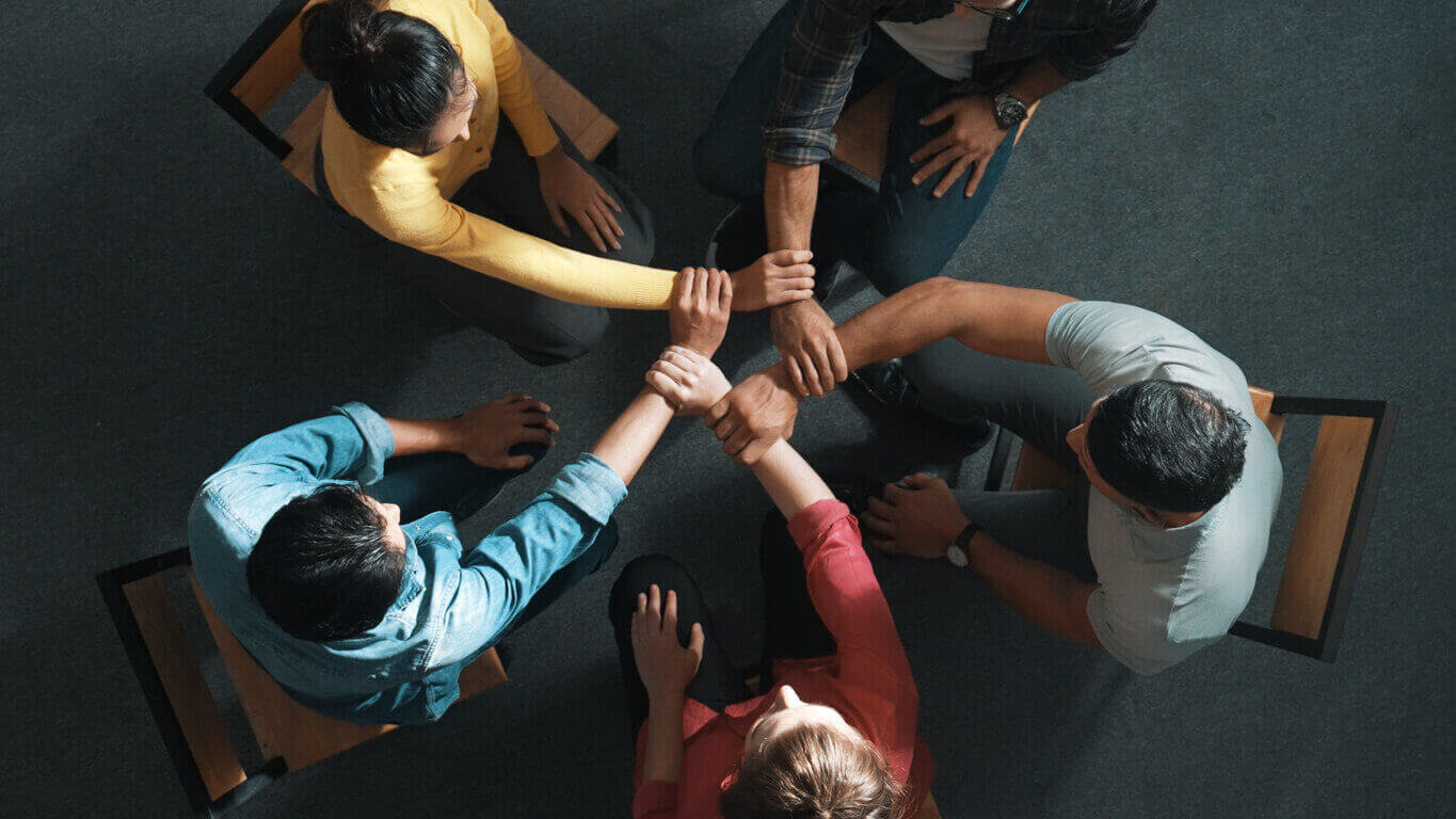 Equipe unida em círculo dando as mãos, representando práticas colaborativas e eficazes de gestão de pessoas no ambiente corporativo.