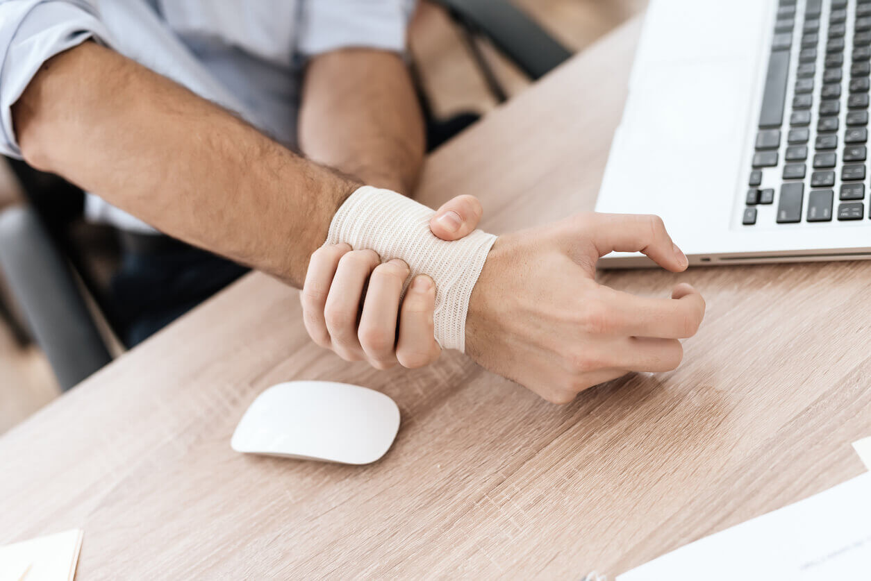 Homem com o punho enfaixado trabalhando no computador, ilustrando a importância da Prevenção de Acidentes do Trabalho em ambientes corporativos