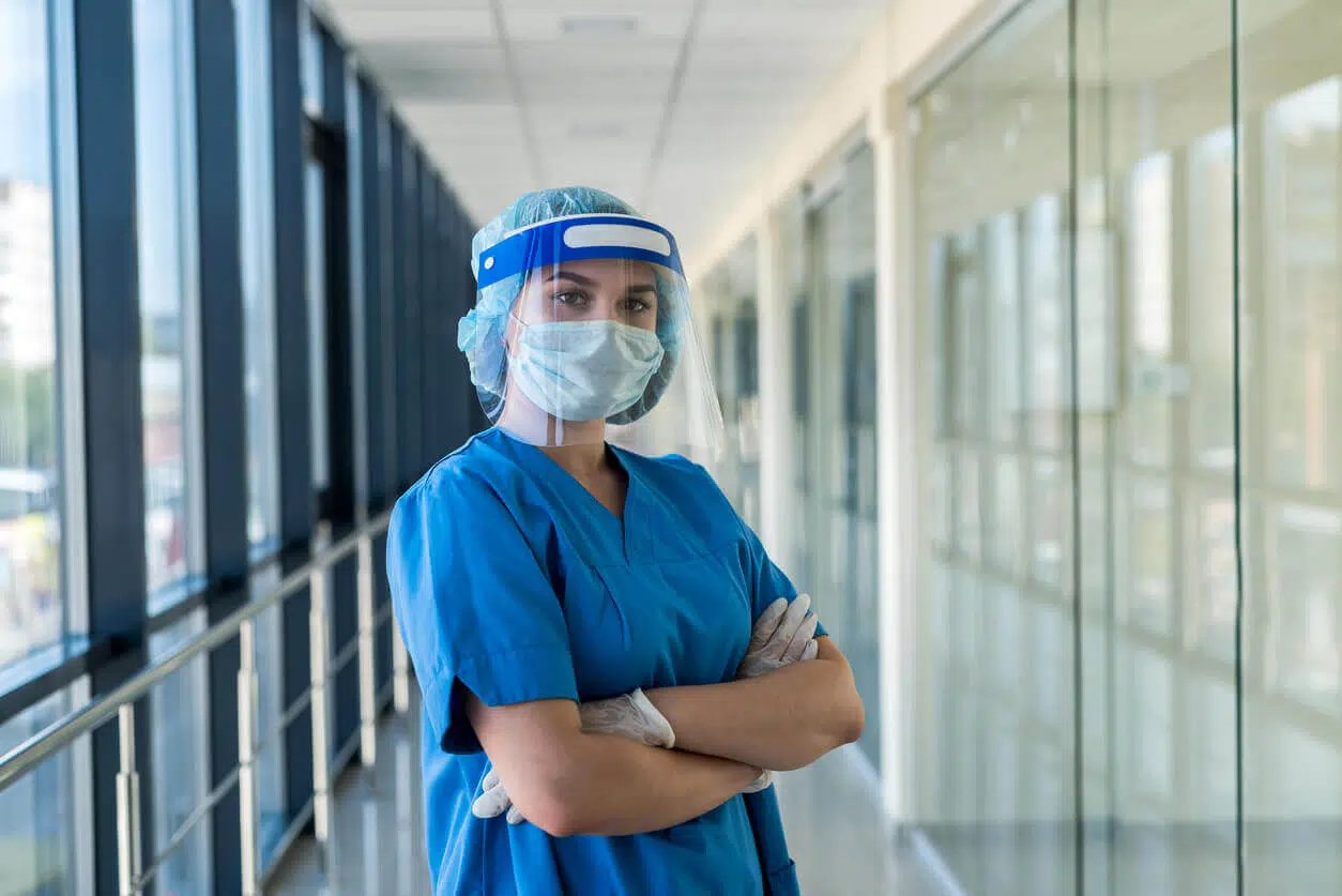 Profissional da saúde utilizando equipamentos de proteção individual em corredor hospitalar, exemplificando a aplicação das normas de SST no ambiente de trabalho.