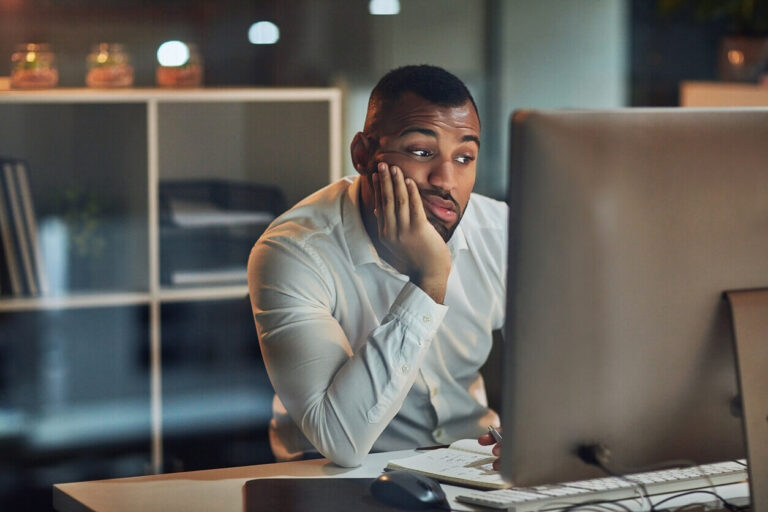 Homem entediado olhando para o computador no trabalho, ilustrando os impactos da síndrome de boreout na motivação e saúde mental