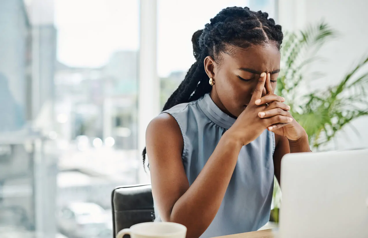 Mulher com expressão de cansaço no ambiente de trabalho, ilustrando a importância da prevenção do burnout e dos cuidados com a saúde mental no dia a dia profissional.